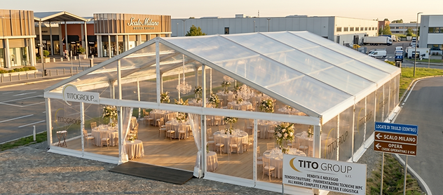 Elegante tendostruttura Bifalda Crystal trasparente di Tito Group S.r.l. allestita a Locate di Triulzi, in prossimità di Scalo Milano. L'interno mostra la pavimentazione tecnica professionale in legno chiaro originale dell'azienda, con allestimento per eventi e gala. In primo piano, il cartello ufficiale con il logo Tito Group e indicazioni stradali per Locate Centro, Scalo Milano e la sede operativa di Opera a 2 km.