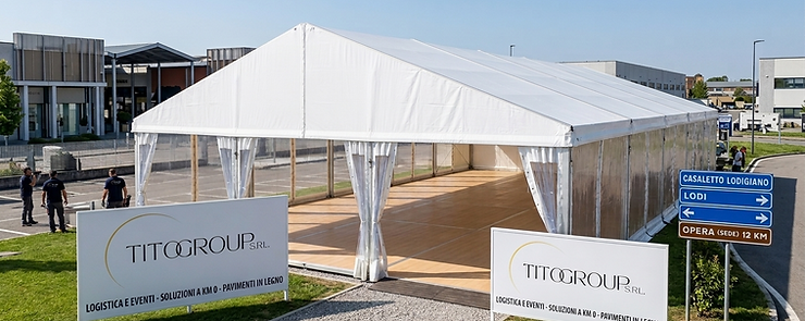 Tendostruttura professionale Bifalda bianca di Tito Group S.r.l. allestita a Casaletto Lodigiano. L'interno mostra la pavimentazione tecnica in legno chiaro originale posata a regola d'arte. In primo piano, cartelli pubblicitari con il logo ufficiale Tito Group e indicazioni stradali per Lodi e la sede operativa di Opera a 12 km. Sullo sfondo, un contesto logistico moderno e curato.