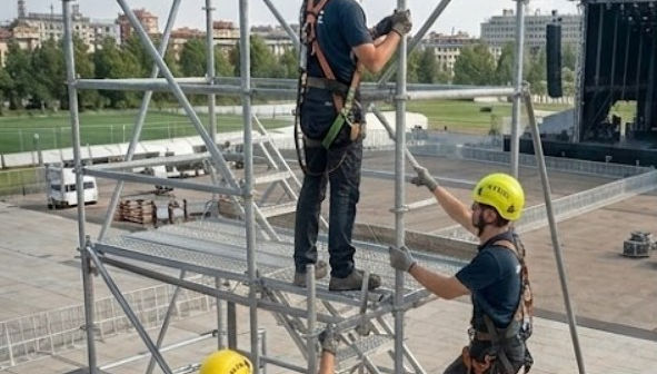 Squadra di tre operai specializzati con caschi Petzl e imbracature di sicurezza mentre montano un ponteggio multidirezionale per un grande palco da concerto all'aperto a Milano