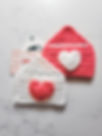 The completed Crochet Heart Envelope Gift Card Holders displayed with gift cards. The yarn colors are white and pink on a white countertop.