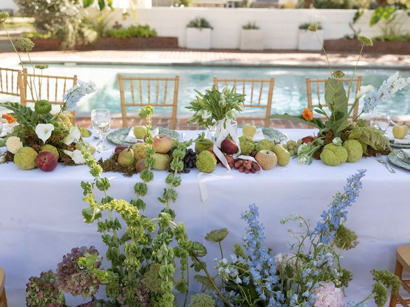 Front view of table set up with colorful florals on the ground and fruit with place settings