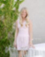 A smiling woman in a light dress stands beside a white-covered table outdoors