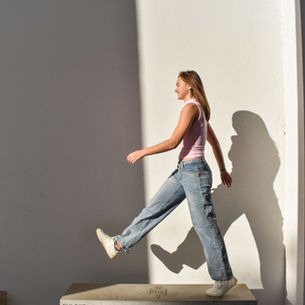 Young woman taking a big step down a sidewalk