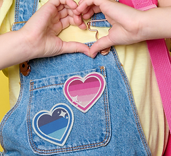 someone wearing a yellow tshirt and blue dungarees. The dungarees have two embroidered patches on the front pocket. One is pink and one is blue.