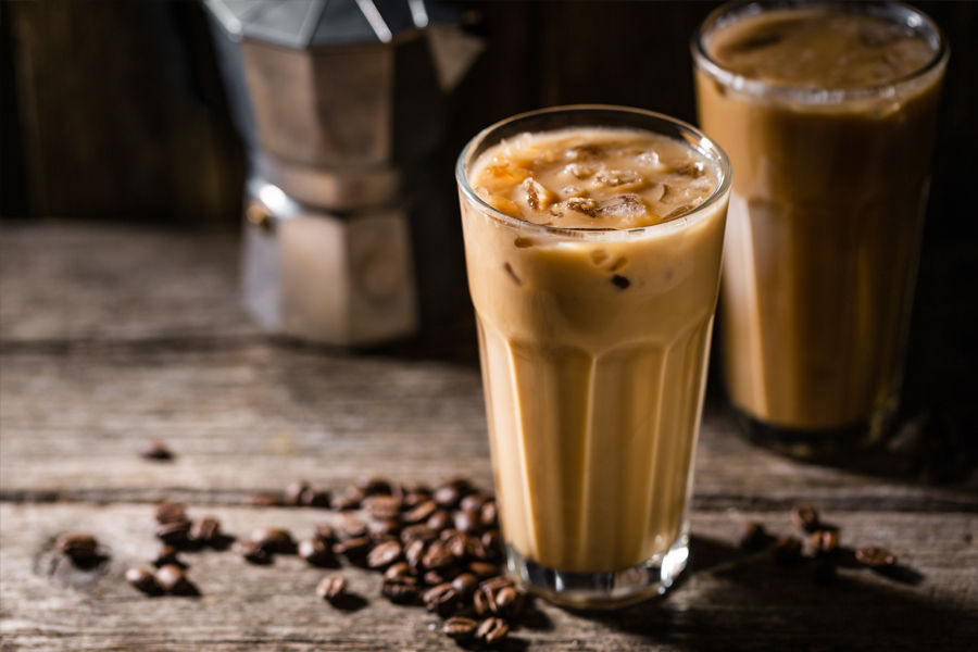 Wooden table top with 2 Iced coffees in a glass with coffee beans and Moka Pot in the background