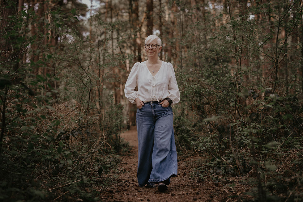 A person in a white blouse and blue jeans walks on a forest path, surrounded by greenery. The scene feels peaceful and natural.