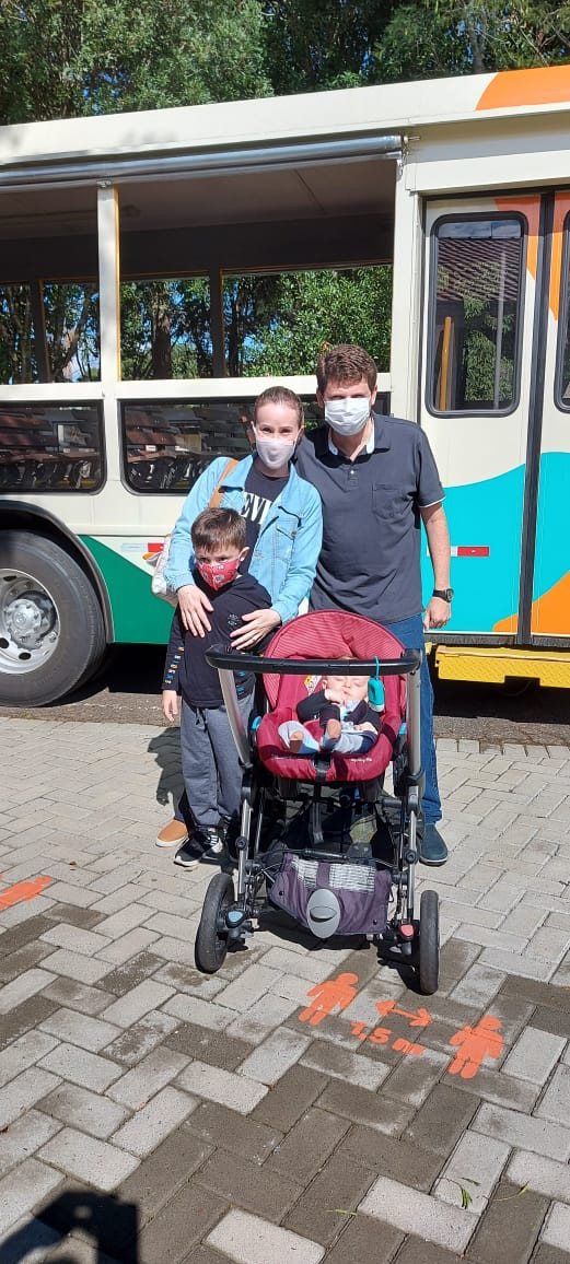 foto da família, sendo 2 adultos, 1 criança e um bebê num carrinho e atrás um ônibus do Parque