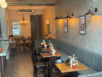 Ambiente interno de cafeteria com mesas de madeira e estofado cinza acolhedor.