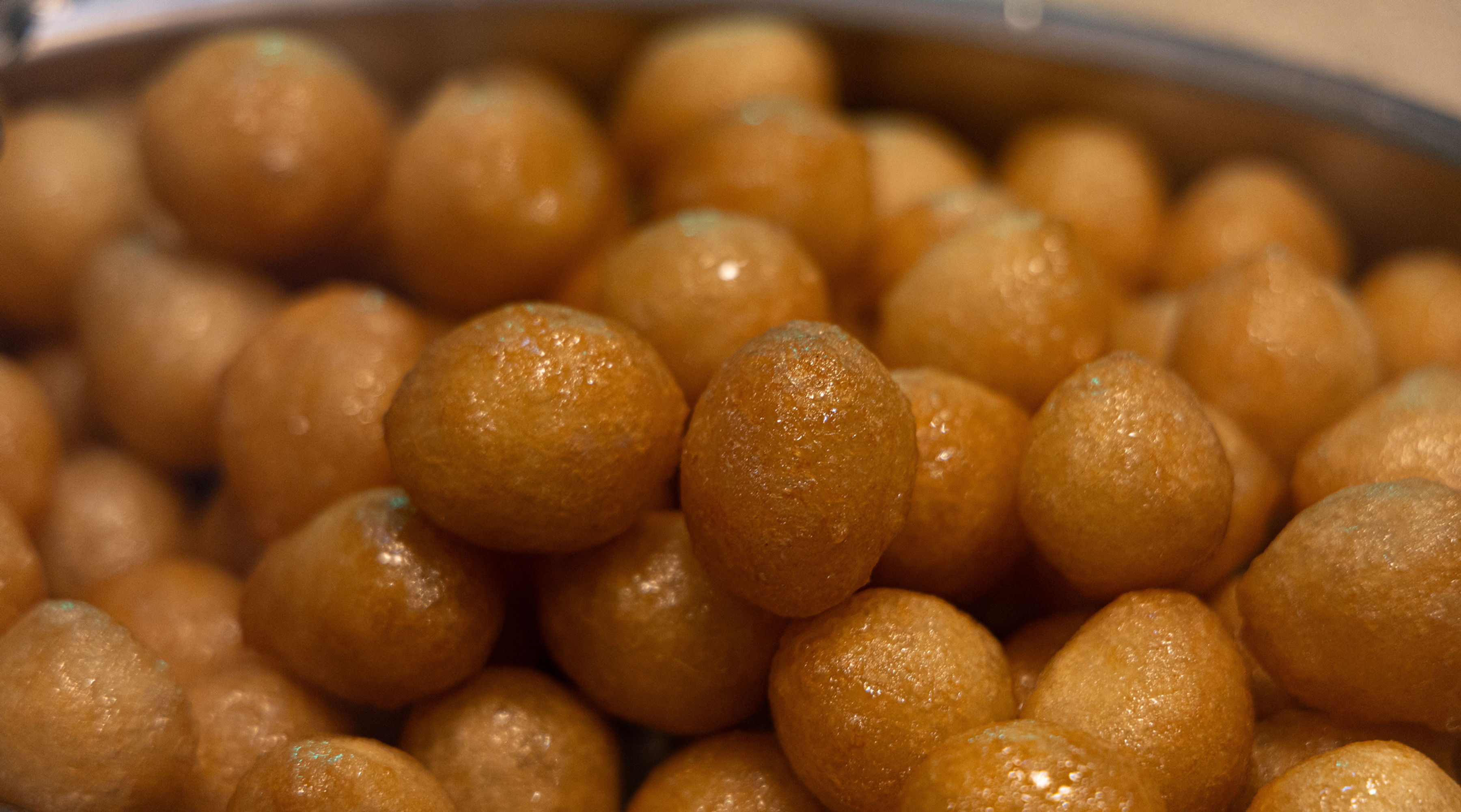 Close-up of a metal bowl filled with glossy golden-brown syrup-soaked dessert balls, piled tightly together.