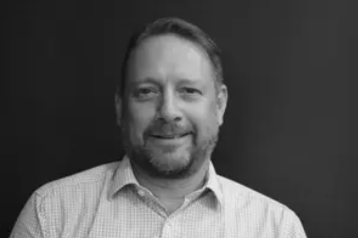 Man in a collared shirt smiling slightly against a plain dark background. Black and white image of Mike Humphreys