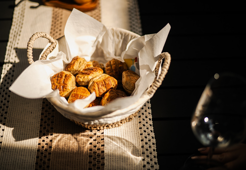 Woven basket of golden croissants on a sunlit table runner, with white napkins and a wine glass creating a warm, cozy breakfast mood. FOODAQUEST food experiences