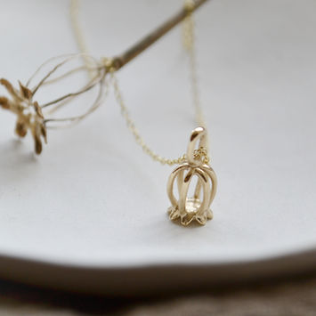 A gold poppy pod pendant on a gold chain.