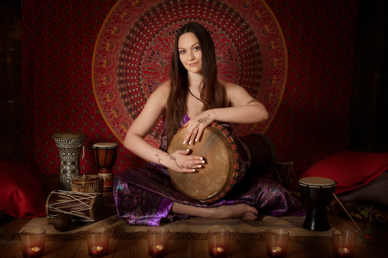 A woman sits on the floor playing a drum