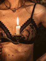 Plan rapproché sur un modèle en lingerie noire tenant un bougeoir allumé. Détail du stage boudoir.