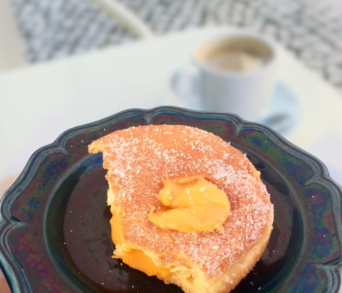 A half eaten bola de berlin on a navy blue ceramic plate topped with an orange dollop of tangerine custard filling