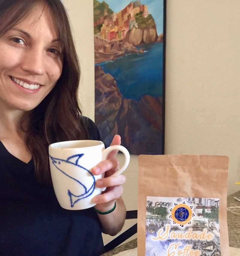 Girl holds cup of coffee next to bag of Saudade Coffee