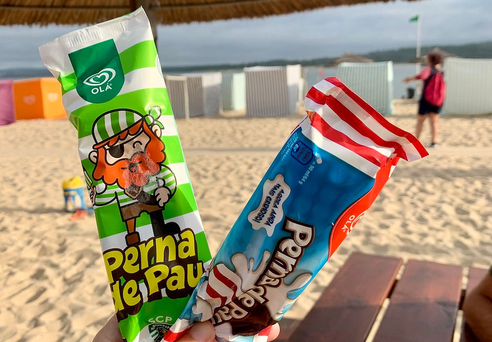 Two Perna de Pau ice creams (one green and one red) being held up with the beach in the background