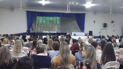 Foto da autora Shirley Souza palestrando para professores em um auditório.