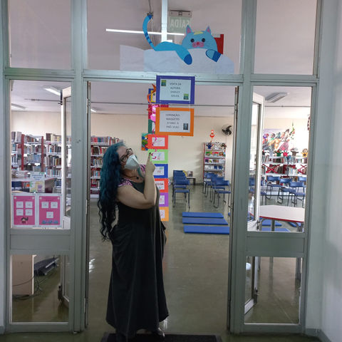 Foto da autora Shirley Souza na entrada da biblioteca da escola, que está decorada com elementos de seu livro Miúdo.