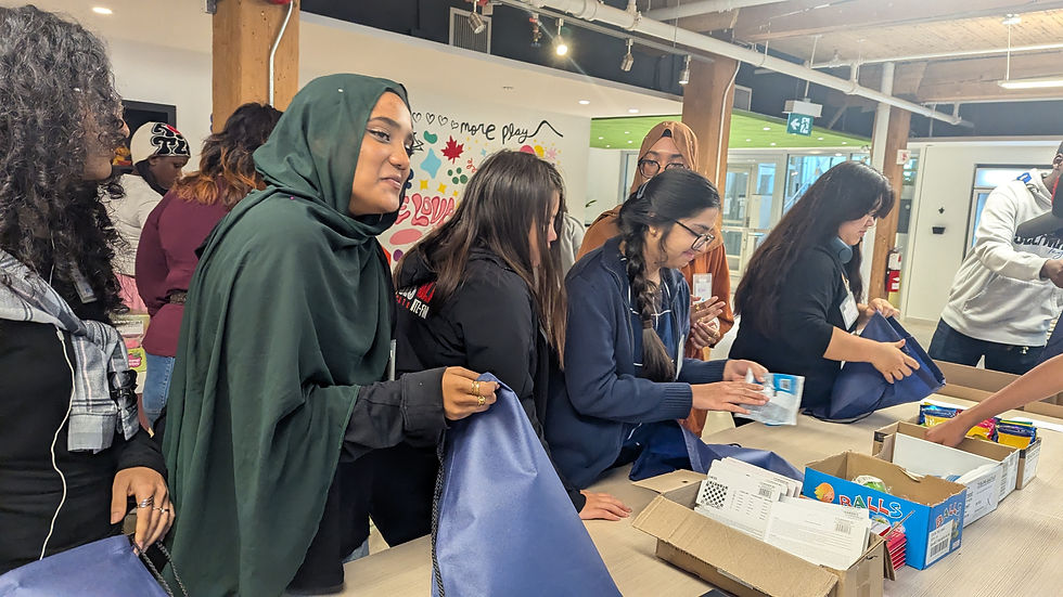 A group of people pack bags with school supplies in a room with colourful wall art. A woman in a green headscarf leads, sharing a joyful mood.