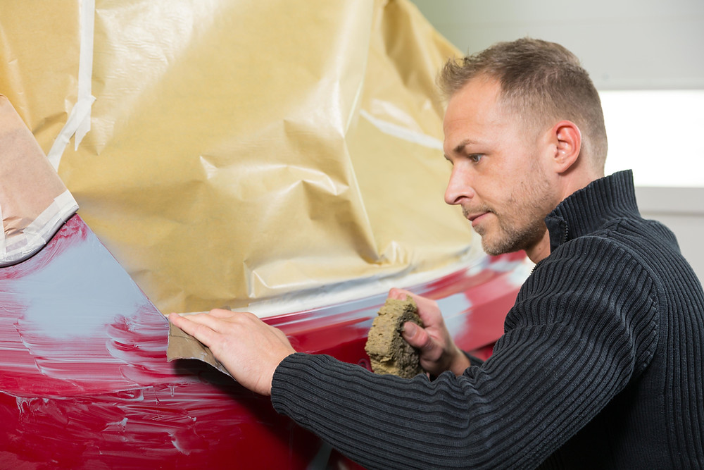man wetsanding a rear bumper of a car