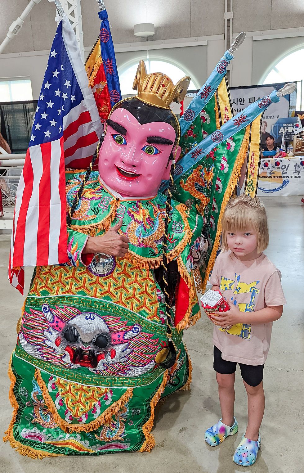 Little girl stands next to traditionally dressed volunteer at Asian Festival