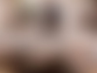 A Sikh kirtan group sits cross-legged beneath stone arches in a gurdwara courtyard, dressed in traditional white clothing and turbans. At the center, a man in a deep blue turban sings into a microphone while playing a harmonium, his expression focused and reverent. Other musicians sit behind him with tabla and attentive postures, as soft daylight filters through the arches, creating a calm, devotional atmosphere rooted in communal prayer and sacred sound.