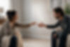 A softly lit cinematic scene of two adults sitting across from each other in a minimalist living room, reaching toward one another with vulnerable expressions as their hands nearly touch. The emotional distance between them reflects attachment needs and longings in Emotionally Focused Therapy, capturing yearning, emotional risk, and the desire for connection and reassurance. Natural daylight and neutral tones create a realistic, intimate atmosphere that emphasizes facial expression and emotional depth.