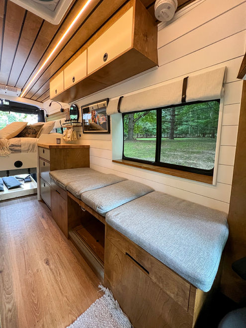 Camper van bed with soft pillows and large window view.