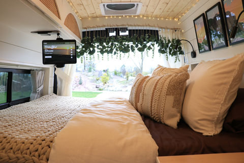 Bed view in Sarah’s Ford Transit Nomadik campervan with iPad on the blanket, CRL Lawrence bunk window, and custom upper cabinets by Drifter Vans
