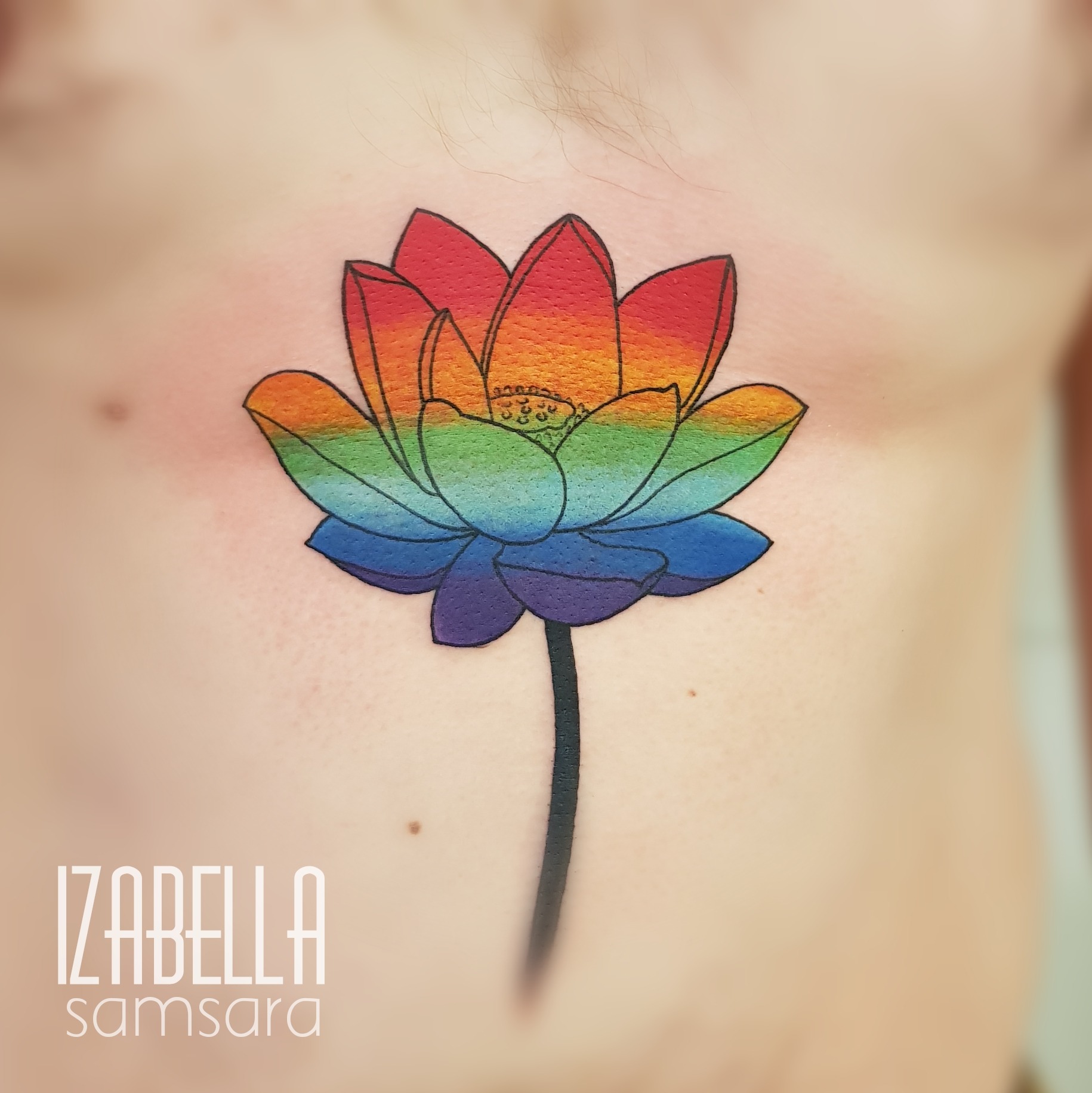 A vibrant lotus flower tattoo featuring a gradient of rainbow colors, with the petals transitioning from red to orange, yellow, green, blue, and purple. The flower is depicted with a black stem, situated on the chest, showcasing intricate detailing in the petals and a serene aesthetic.