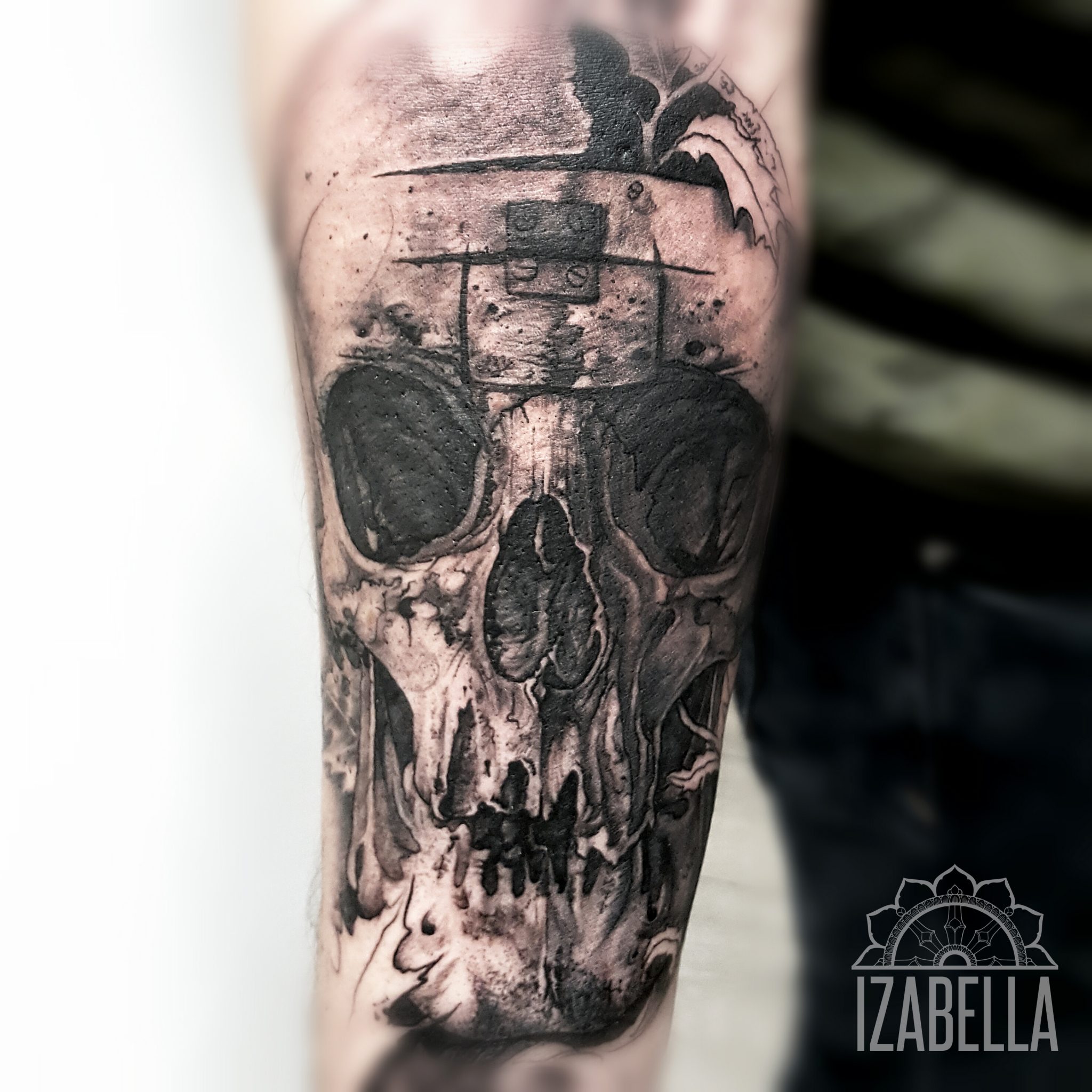 A highly detailed black and grey tattoo of a skull on the forearm, showcasing intricate shading and textures. The skull features dark hollow eyes and a slightly open mouth, with additional elements like smoke and abstract patterns surrounding it, creating a dramatic and artistic effect.