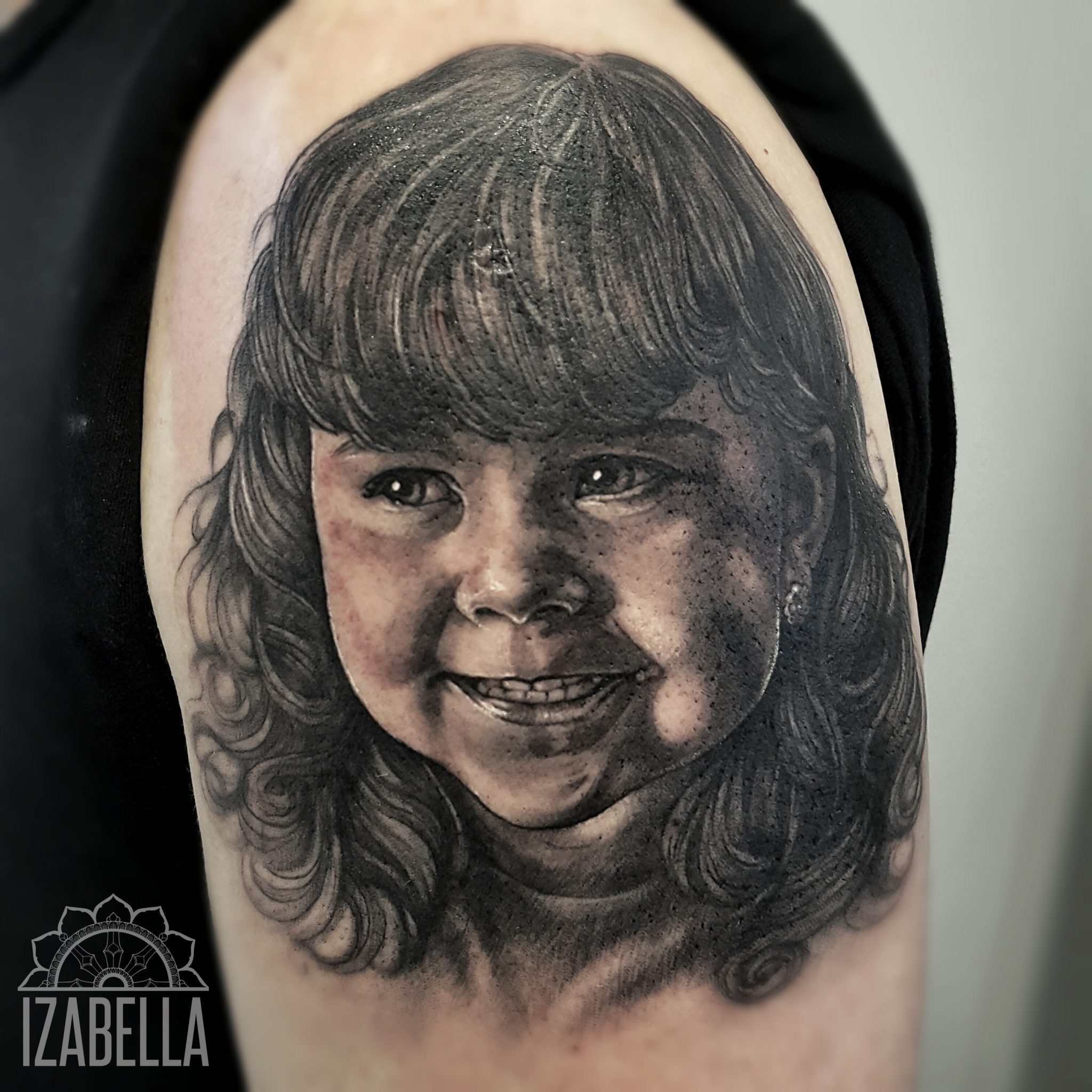 Realistic black and grey tattoo of a smiling young girl with curly hair and a joyful expression, featuring intricate detailing in the facial features and hair.