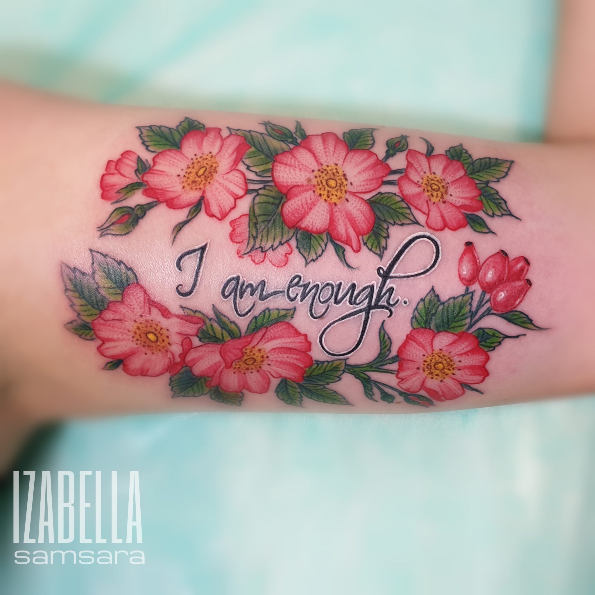 A colorful tattoo featuring vibrant pink flowers with yellow centers and green leaves surrounding the phrase 'I am enough.' This floral design adds a touch of elegance and positivity, making it a meaningful body art piece.