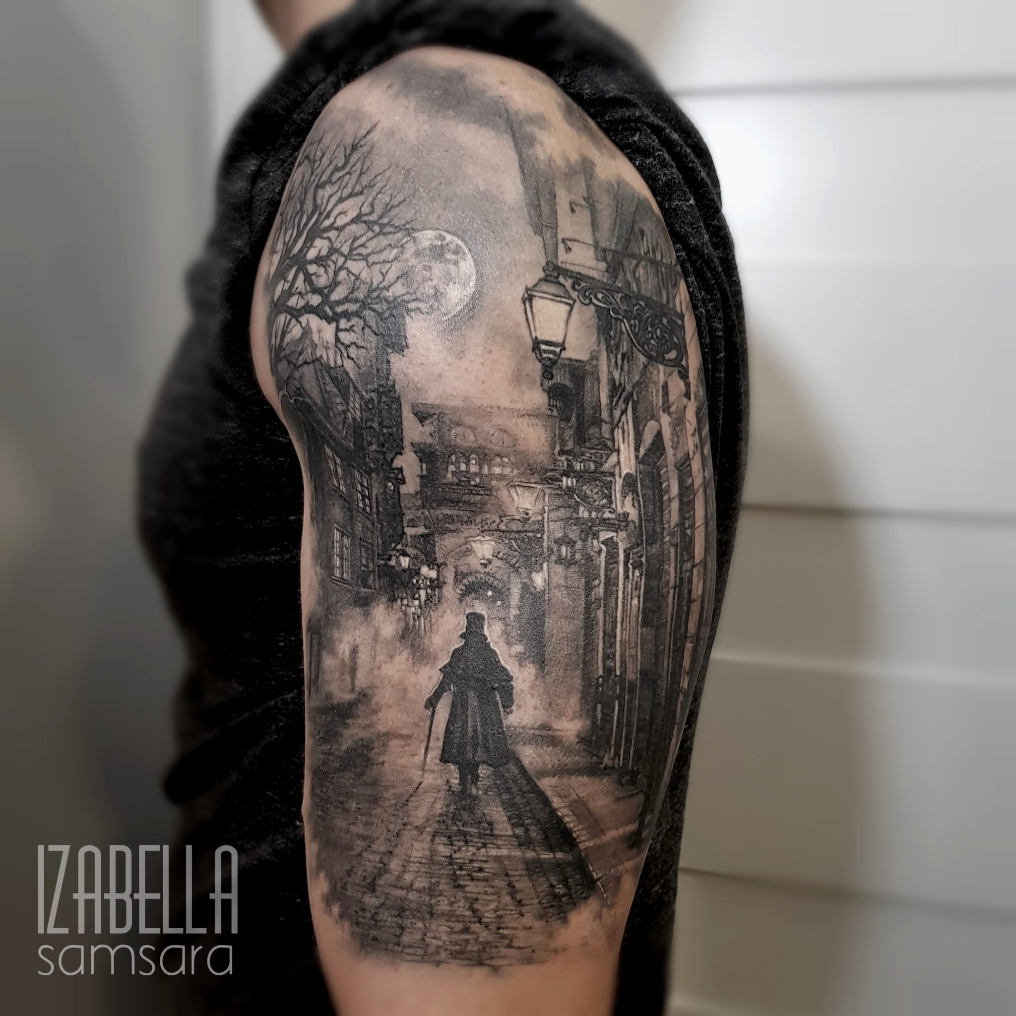 A detailed black and grey tattoo featuring a moody and atmospheric street scene. It depicts a solitary figure in a long coat and top hat walking down a cobblestone path surrounded by vintage street lamps and trees, under a full moon. The background showcases historic architecture, creating a mysterious, almost foggy ambiance.