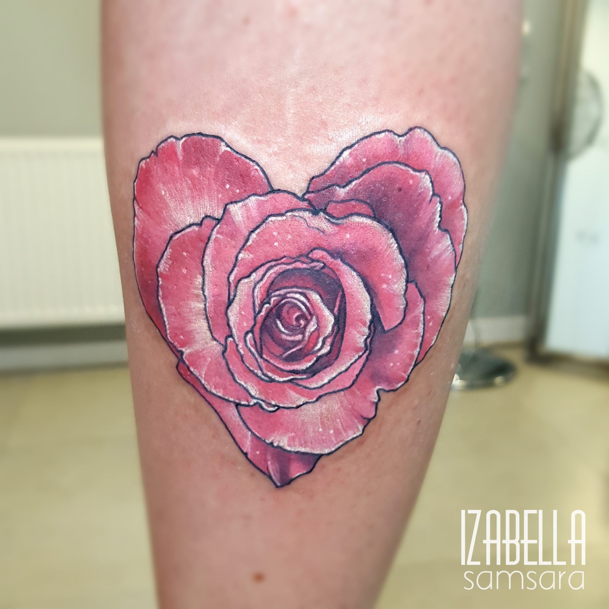 A vibrant pink rose tattoo in a heart shape, intricately designed with shading and details, located on the calf. The tattoo features delicate petals and a realistic appearance, showcasing the artistry of floral ink designs.