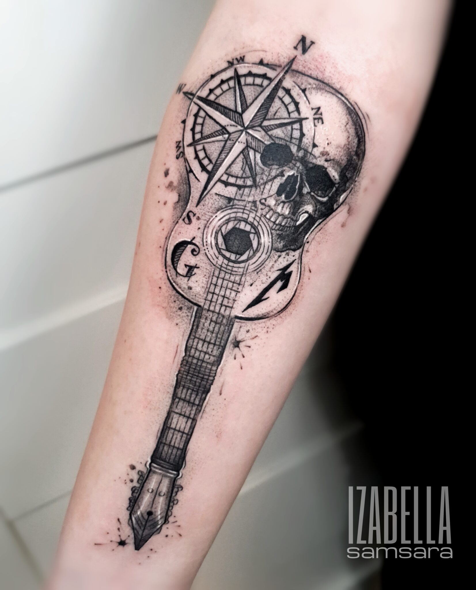 A detailed black and grey tattoo depicting a skull blended with a guitar and a compass. The guitar has an intricate design with visible strings, and the compass rose features cardinal points. Surrounding the design are splatters of ink, adding a dynamic effect. This unique tattoo combines elements of music and navigation, showcasing artistry and depth.