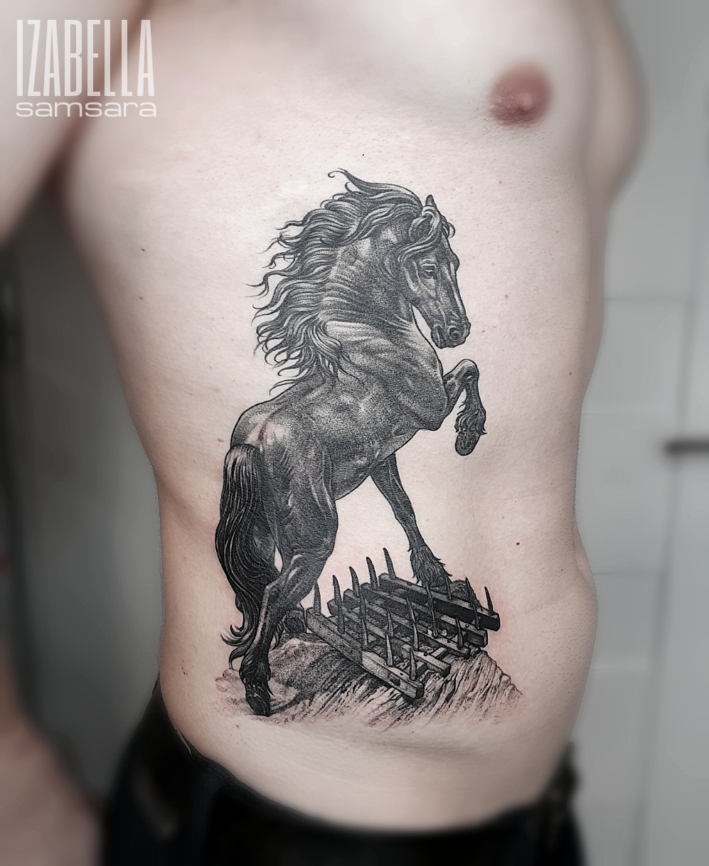 A detailed black and white tattoo of a rearing horse on a textured surface, surrounded by a fence of pointed stakes, emphasizing the horse's muscular physique and flowing mane.