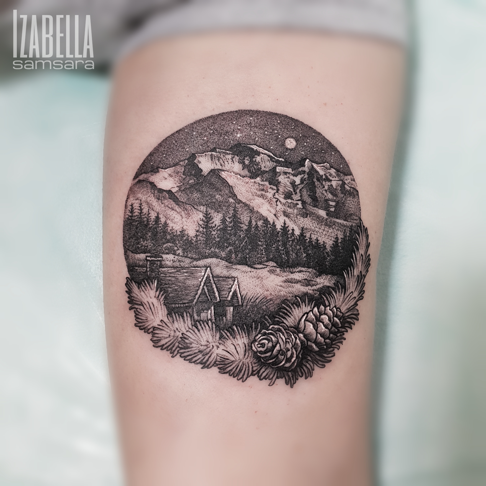 A detailed black and gray tattoo depicting a serene mountain landscape inside a circular frame. The design features towering mountains, a starry night sky, a crescent moon, and dense pine forests in the foreground. At the bottom, there are stylized pine cones and leafy ferns framing the scene, along with a sketch of a small cabin, creating a tranquil and nature-inspired artwork.