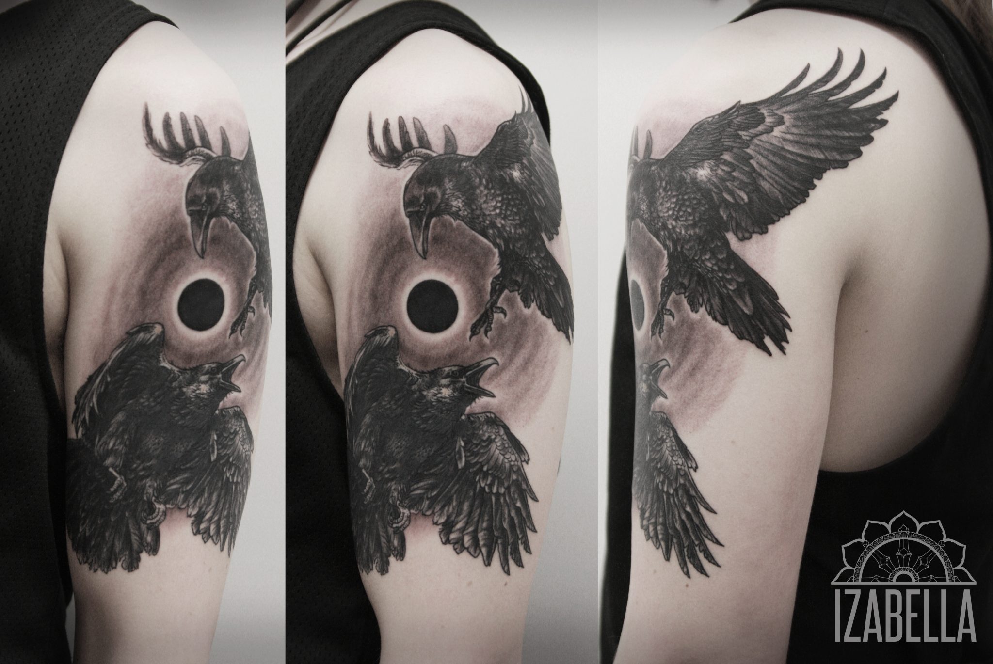 A detailed black and gray tattoo featuring two ravens. One raven is soaring with its wings spread wide, while the other is captured in a vocal pose. The background includes a dark circle surrounded by a soft, shaded halo effect, creating a mystical ambiance. This artwork is intricately designed and placed on the upper arm, showcasing fine lines and shading techniques.