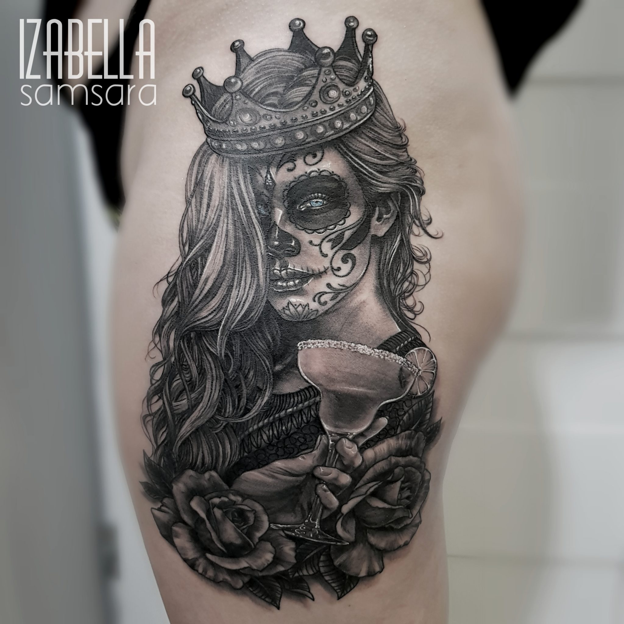 A detailed black and gray tattoo featuring a beautiful woman with a crown, inspired by the Day of the Dead. Her face is decorated with intricate floral patterns typical of sugar skull art. She is holding a margarita glass garnished with a lime, surrounded by roses. The tattoo showcases fine line work and shading, emphasizing the elegance and intricacy of the design.