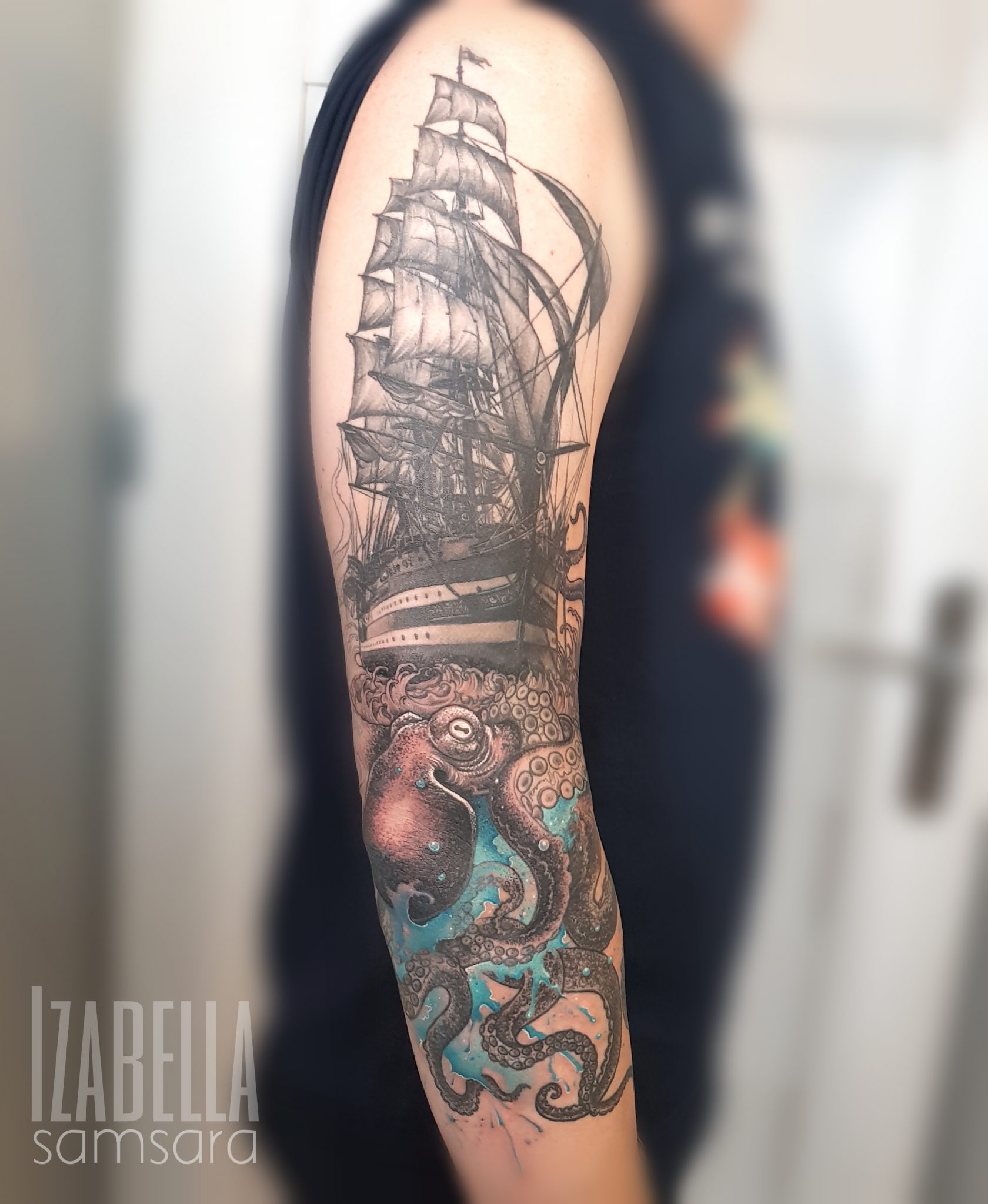 A detailed tattoo of an octopus entwined around a ship, showcasing a dramatic black and gray design with hints of vibrant blue, creating an eye-catching nautical theme on the arm.