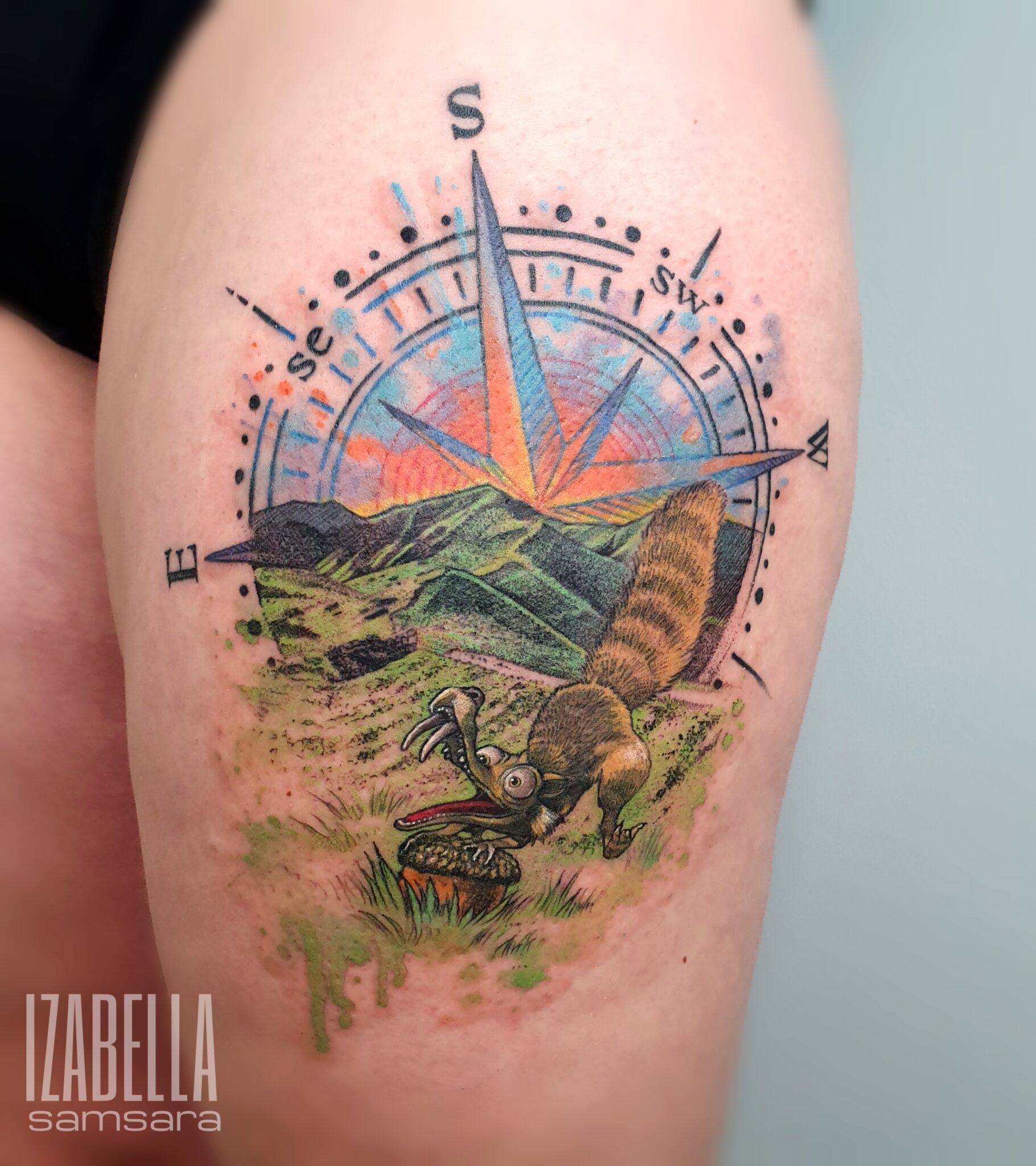 A colorful tattoo featuring a playful creature resembling a cartoonish rodent, positioned in a green landscape with mountains in the background. The creature is depicted with a vibrant, expressive face and is standing on a rock, next to a compass design that includes cardinal directions and a rising sun. The design uses bold colors like greens, oranges, and blues, making it eye-catching and whimsical.