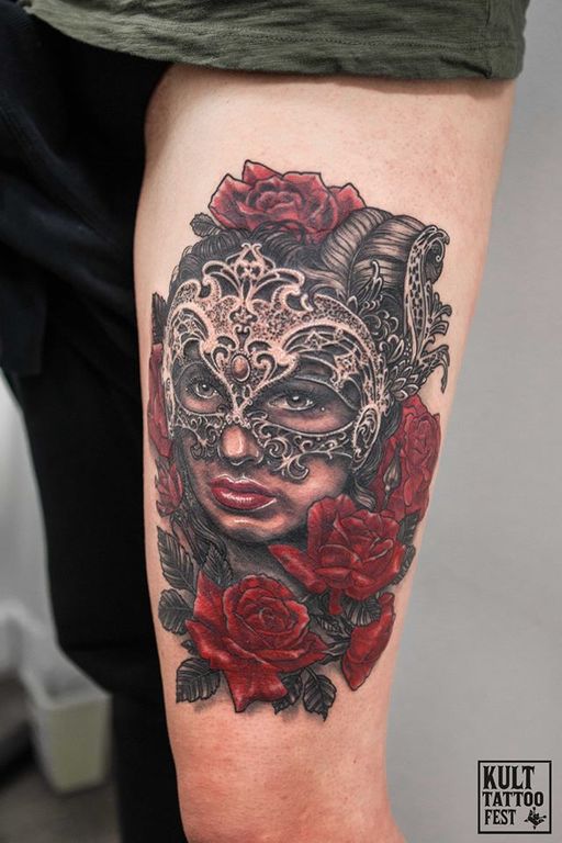 A vibrant tattoo featuring a woman's face partially concealed by an ornate masquerade mask, surrounded by lush red roses. The detailed design showcases intricate patterns on the mask and lifelike facial features, highlighting the contrast between the delicate mask and the bold flowers.
