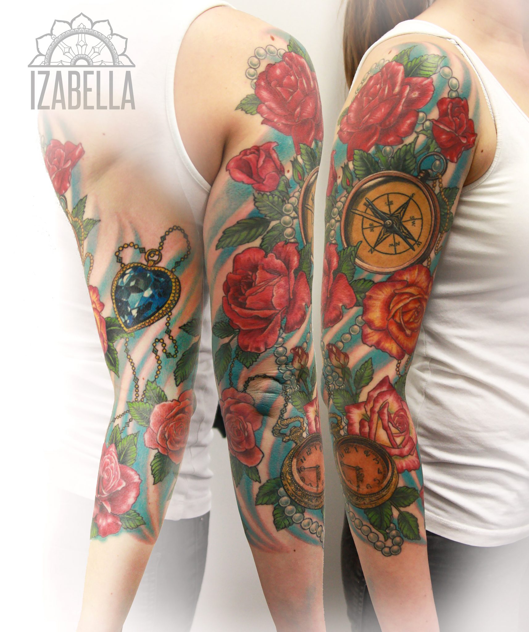 A vibrant tattoo featuring large red roses, a blue heart-shaped gem, a vintage compass, and a clock with Roman numerals, embellished with pearl-like beads and green leaves. The design is rich in color, wrapping around the arm and creating a visually striking sleeve.