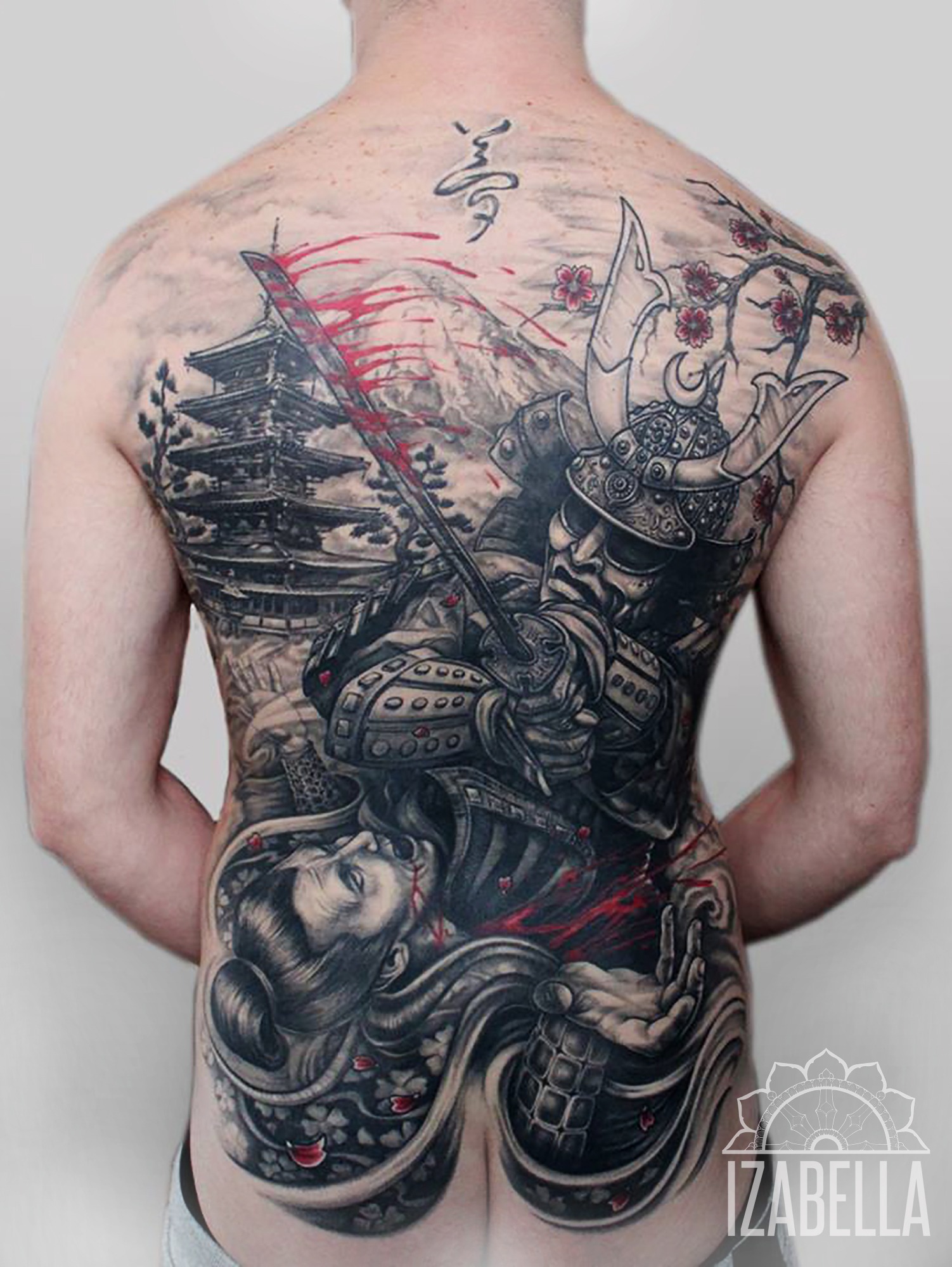 A detailed black and gray tattoo depicting a samurai warrior in traditional armor engaged in battle, with a flowing red blade and elements of Japanese cherry blossoms and a pagoda in the background. The tattoo covers a person's entire back, illustrating a dynamic scene with intricate shading and patterns, showcasing elements of Japanese culture and artistry.
