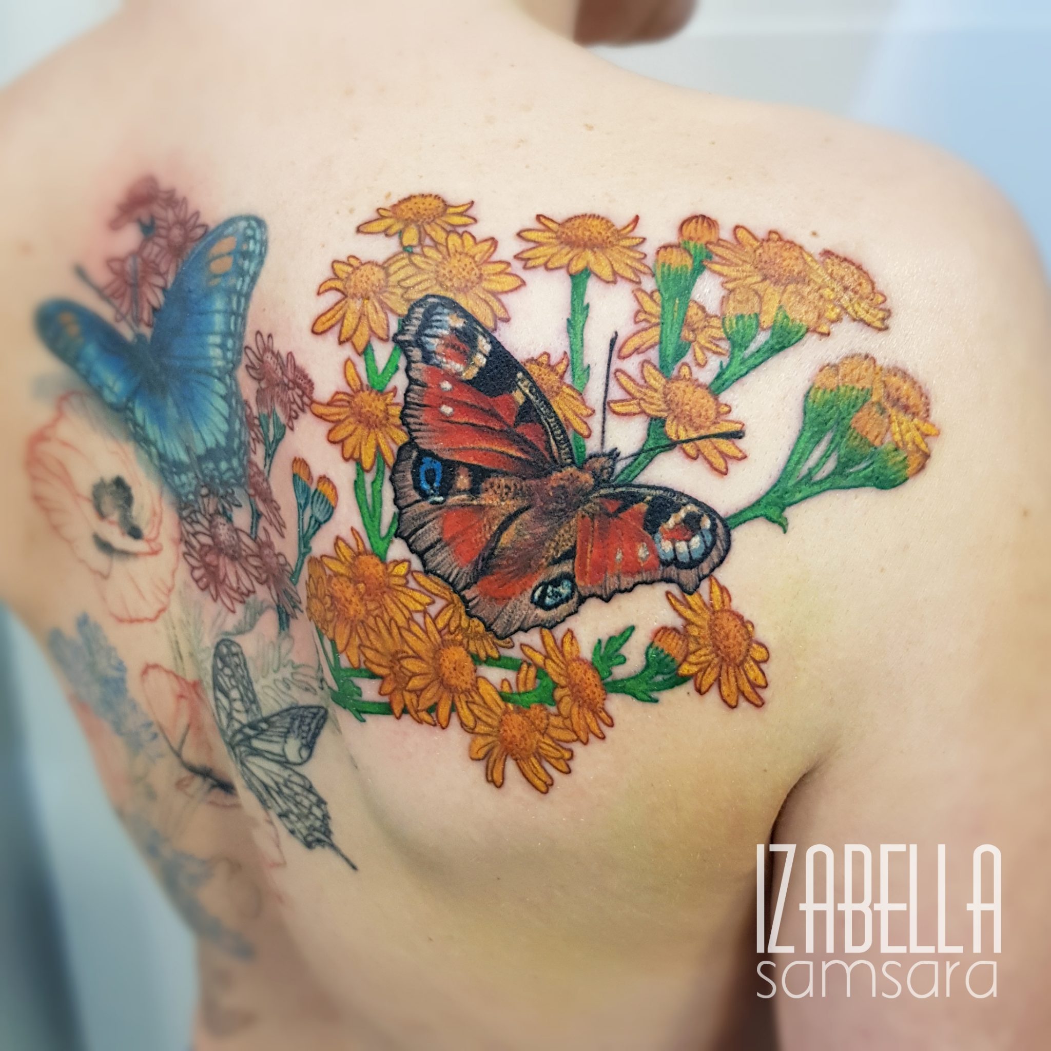 Colorful tattoo featuring a large peacock butterfly surrounded by vibrant yellow flowers and green leaves on the upper back, showcasing intricate details and a lively composition.