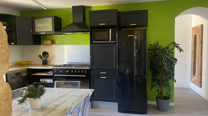 Rénovation de cuisine moderne avec meubles noirs mats, mur vert accent, électroménager intégré et table en bois clair, aménagement contemporain fonctionnel et lumineux.