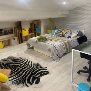 Chambre sous pente rénovée avec poutres peintes en blanc, sol chaleureux et mobilier intégré.
