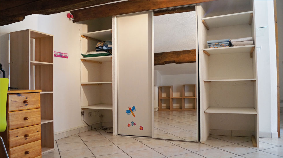 Ancien espace dressing sous pente avec placard coulissant, étagères ouvertes et sol carrelé clair avant travaux.